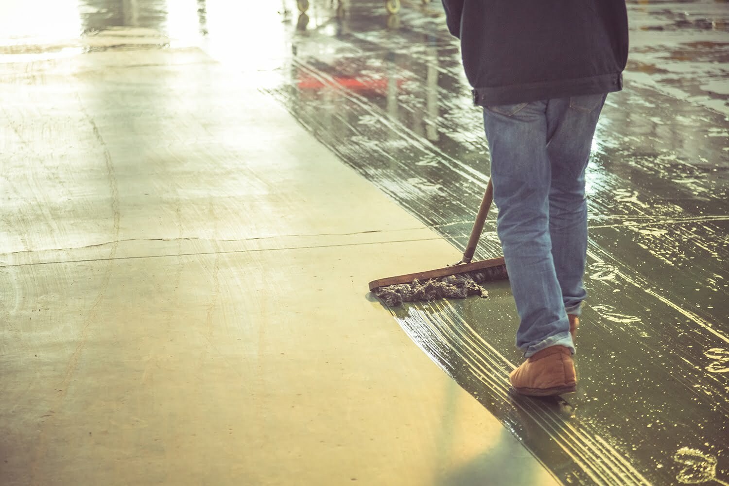 low section of male worker mopping the concrete floor in factory