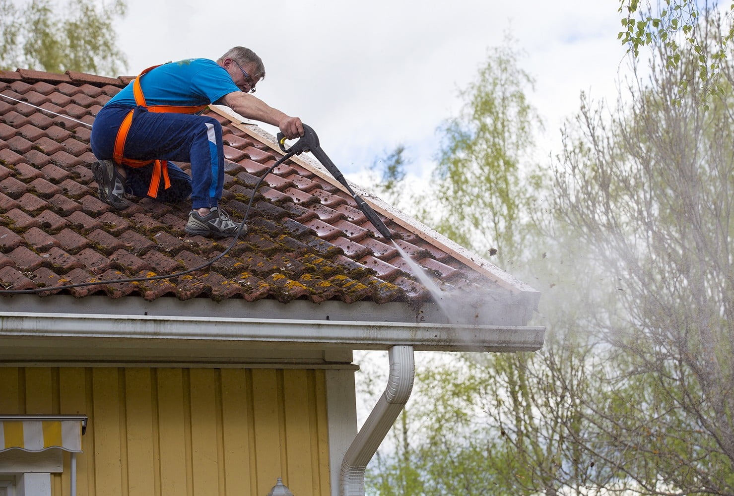 Caucasian man is washing the roof with a high pressure washer. H tile roof power washing